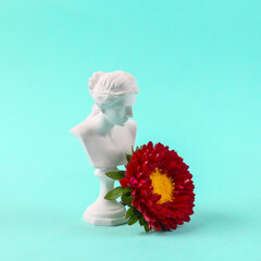 Plaster bust of venus with a flower on blue background.
