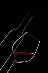 Glass and bottle of red wine on a black background.