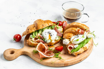 Croissant with prosciutto, poached egg, jamon, blue, cheese, avocado, microgin and cherry tomatoes. Mediterranean appetizer. Breakfast concept