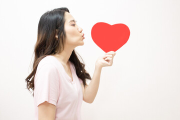 Fototapeta na wymiar Asian beautiful woman are holding red heart shape paper and do blow kiss with happiness. A Valentine day and Love.