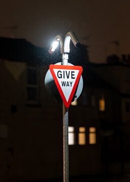 Give way traffic sign brightly illuminated at night in dark. LED lights shining on triangle signage warning traffic of bust junction in darkness.
