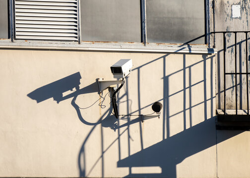 CCTV professional camera looking out with shadow cast on building wall. High security area with closed circuit television camera, stairway and industrial building.