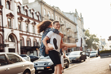 Couple in love. Man carrying girl on his back in the street. Smiling man with beautiful young woman, ride piggyback, having fun together. Relationship concept.