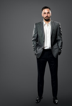 Fashion Handsome Bearded Man in Gray Suit and White Shirt without Tie. Elegant Businessman in Open Collar Shirt, Hands in Pocket Full Length over Gray Background
