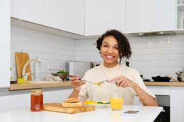 Smiling african american woman having traditional breakfast with fried egg and fresh vegetables