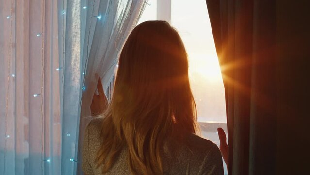 Young woman watches sunset trough the window