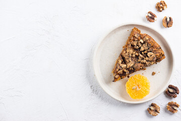 A piece of homemade mandarin pie with walnuts in a plate. Sugar, gluten and lactose free, vegan. Horizontal orientation, copy space, top view.
