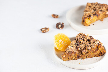 Pieces of homemade pie with tangerines and walnuts on a light table. Sugar, gluten and lactose free, vegan. Horizontal orientation, copy space.