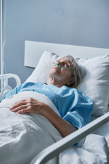 Senior woman with oxygen tube in her nose lying in bed at hospital ward