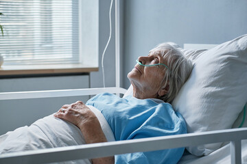 Senior woman with oxygen tube in her nose resting on the bed during her treatment at hospital