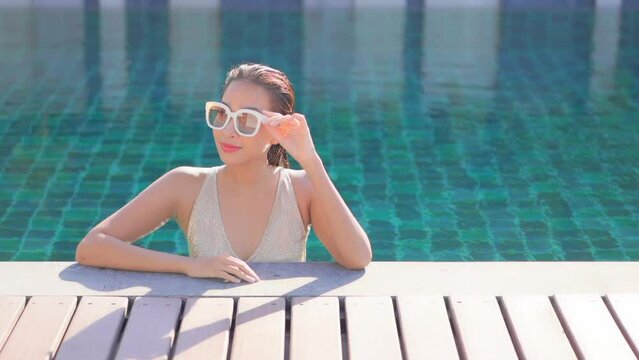Sexy smiling asian woman in swimming pool on hot sunny summer day, vacation concept, slow motion