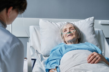 Senior woman listening to the recommendations of her doctor while she lying on bed at hospital ward