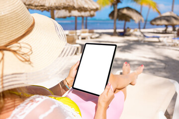 Woman on tropical beach holding tablet in vertical screen orientation, blank tablet's screen mockup