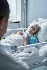 Obraz premium Sick senior woman listening to her doctor while she lying on bed at hospital ward