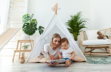 Happy woman mom and her little daughter read book in wigwam at home © splitov27
