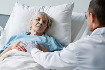 Senior woman sleeping on her hospital bed while doctor treating and caring about her at the ward