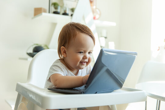 Little funny baby uses a laptop while sitting at the children's table at home