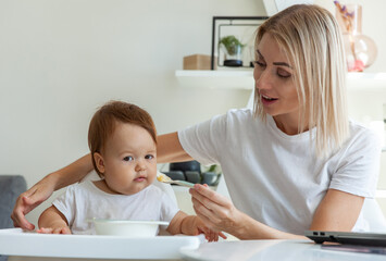Obraz premium A caring mother feeds her baby from a spoon while sitting at a table