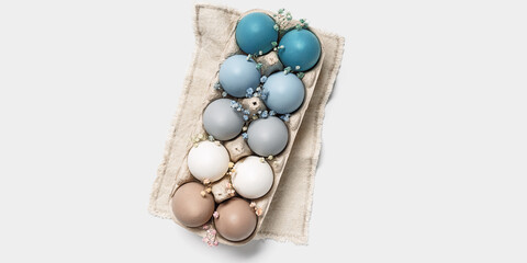 Easter eggs pastel colored in egg box decorated small flowers. Minimal Easter celebration concept, dyed chicken egg with color gradient from blue to beige coloured in carton pack. Top view