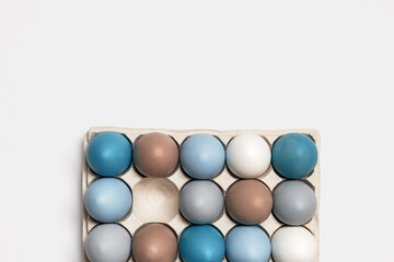 Colorful Easter eggs in carton packing, blue, beige, white neutral colors, festive chicken egg in paper container on lihgt grey colored background. Minimal style aesthetic composition