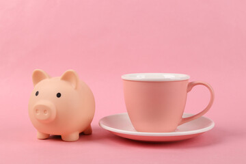 Fototapeta na wymiar Empty ceramic cup with piggy bank on pink background