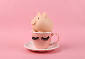 Ceramic cup with false eyelashes and piggy bank on a pink background. Minimalistic creative shot