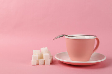 Empty ceramic cup with sugar cubes on pink background