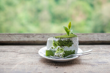 Green tea cake with young bud tea leaf on wooden table against tea garden background