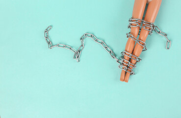 Concept about abusive relationships. Doll's legs wrapped in a chain on a blue background