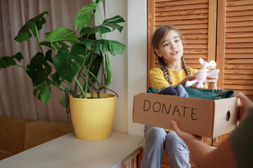 Mother with daughter sort out the wardrobe and collect clothes and toys for donate box at home....