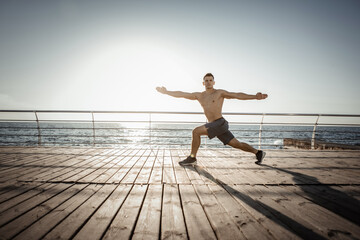 Fototapeta premium Young muscular man practicing yoga asana at sunrise on the beach