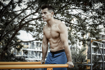 Handsome man athlete workout outdoors. The guy does push-ups on the uneven bars. Healthy lifestyle