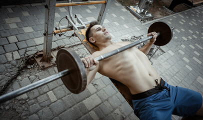 Muscular man doing barbell bench press on a bench outdoors. Healthy lifestyle. Outdoor training
