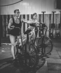 Two muscular athletic women exercising on air bikes at the gym. Functional training cross class working out
