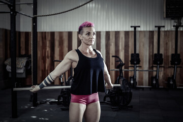 Obraz na płótnie Canvas Extraordinary muscular powerful woman with pink hair is practicing warm-up before intense workout in a modern cross-gym.