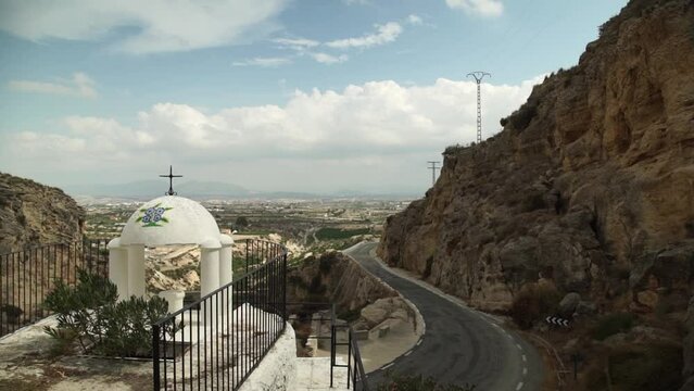 Small white cupula Christian cross in Spain by side road, static, windy day
