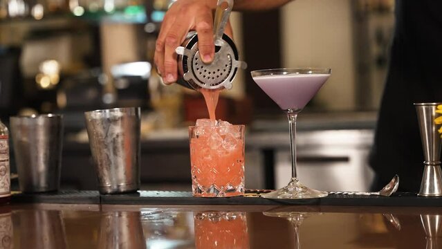 Colorful orange cocktail being poured by bartender into rocks glass slow motion 4k 30p