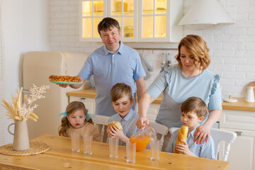 Large family with teenage children eating breakfast in kitchen. Caucasian parents and children decided to have snack and drink fresh juice at home in kitchen. Happy caucasian kids and mom with dad