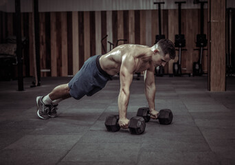 Muscular powerful man doing push-ups with dumbbells in gym