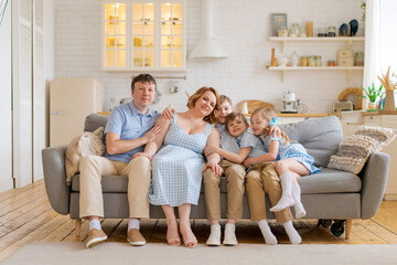 Big happy family sitting on sofa in living room, happy and joyful smile. Family love concept. Caucasian parents spend time with two sons and a daughter. Complete happy family of five