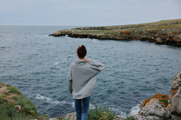 Fototapeta na wymiar woman in a gray sweater stands on a rocky shore nature Relaxation concept