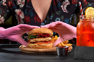 Woman in pink rubber gloves taking hamburger with pork steak