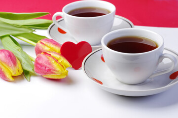 Two cups of tea, a red heart and a bouquet of tulips on the table.