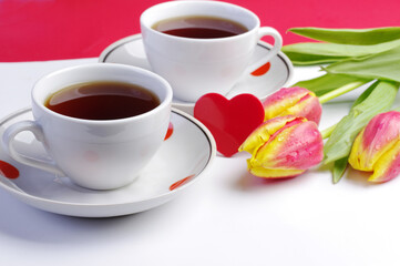 Fototapeta na wymiar Two cups of tea, a red heart and a bouquet of tulips on the table.