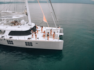 A cruise drone's brilliant photo of a white gorgeous yacht on an open sea with several young females in swimsuits. Fun dancing on board. ..Relaxing on yacht. The concept of enjoying party.