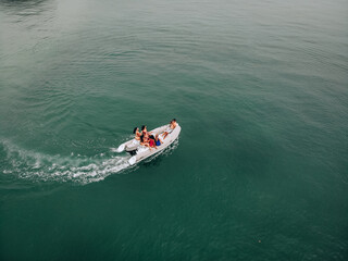 Tourist aerial photography on the open clear turquoise sea. A young guy conducts a photo session for young pretty girls in swimsuits on a white motor boat. Group posing for the camera.