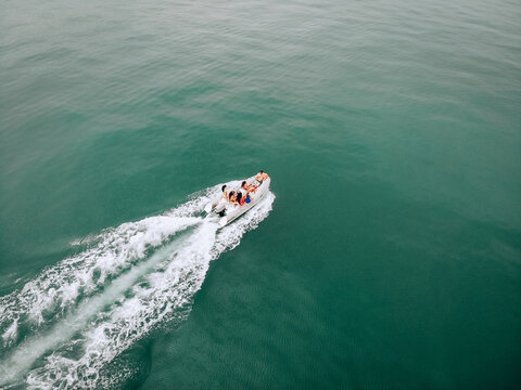Drone's image in open space at sea. Young people sail on a white motor boat on a hot summer day. Beautiful young womens in swimsuits communicate with a guy in a black cap and a camera in his hands.