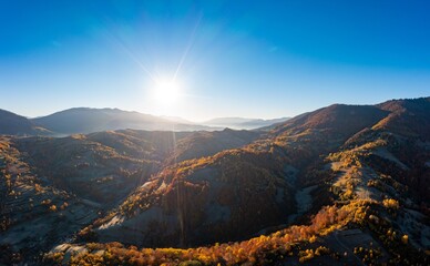 Sun rises above high mountain peaks with yellowed trees