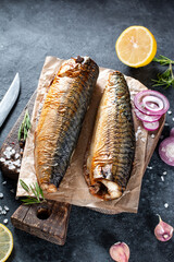 Delicious smoked fish mackerel on paper with garlic and onion. On rustic background