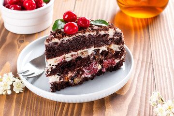 A piece of chocolate cake with cherry on plate on a wooden table.